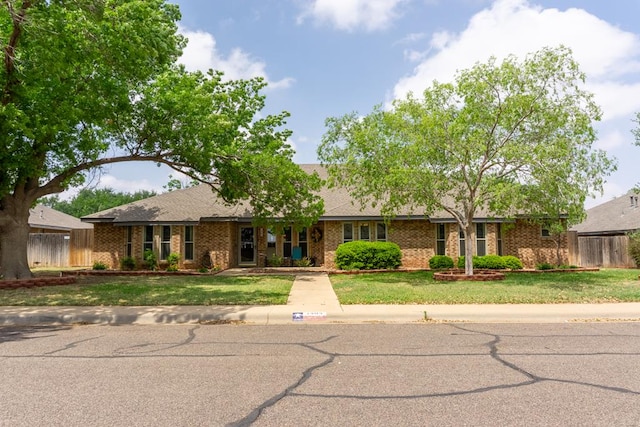 ranch-style home with brick siding, a shingled roof, a front lawn, and fence