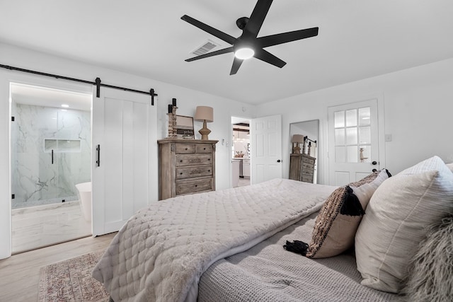 bedroom with ceiling fan, a barn door, light wood-type flooring, and ensuite bath