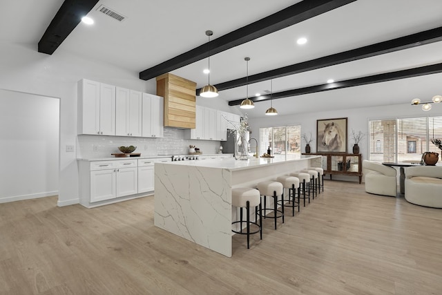 kitchen featuring light hardwood / wood-style flooring, white cabinetry, hanging light fixtures, a spacious island, and tasteful backsplash