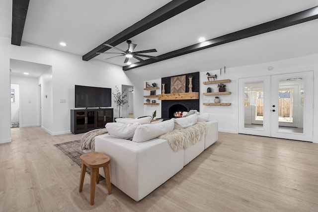 living room with ceiling fan, beam ceiling, a fireplace, french doors, and light wood-type flooring