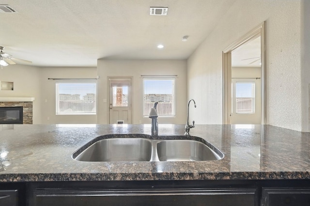 kitchen with a sink, ceiling fan, open floor plan, dark stone counters, and plenty of natural light