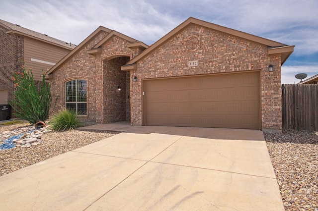 view of front of home with brick siding, concrete driveway, an attached garage, and fence