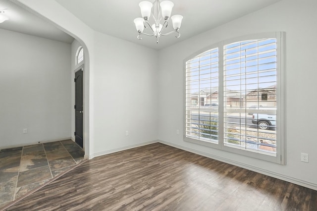 empty room featuring healthy amount of natural light, a chandelier, baseboards, and wood finished floors