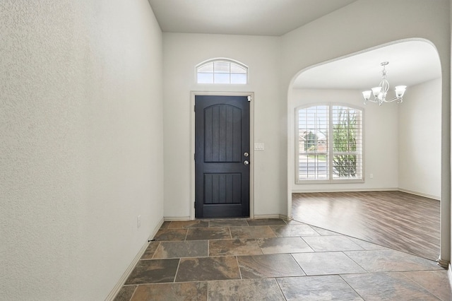 entrance foyer featuring healthy amount of natural light, arched walkways, a chandelier, and baseboards