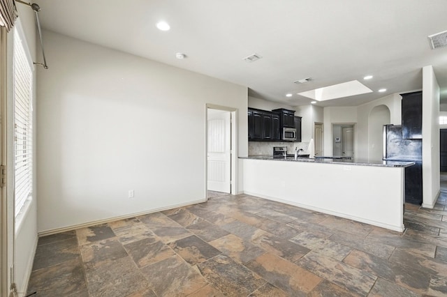 kitchen featuring stainless steel microwave, stone tile flooring, arched walkways, a peninsula, and a skylight