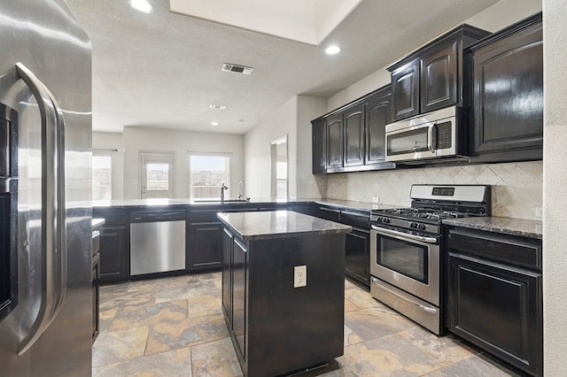 kitchen with appliances with stainless steel finishes, stone tile floors, decorative backsplash, a center island, and dark stone countertops