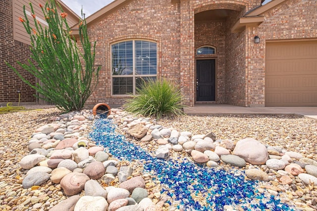 view of exterior entry featuring brick siding, an attached garage, and driveway