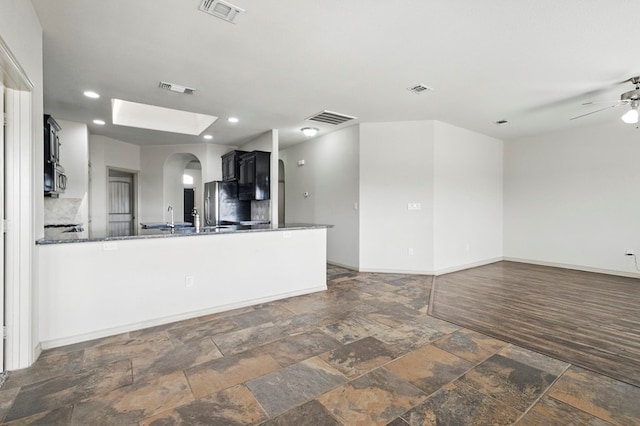 unfurnished living room featuring stone tile flooring, arched walkways, baseboards, ceiling fan, and a skylight