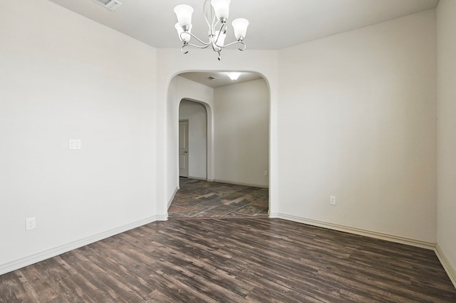 empty room featuring dark wood finished floors, arched walkways, a chandelier, and baseboards