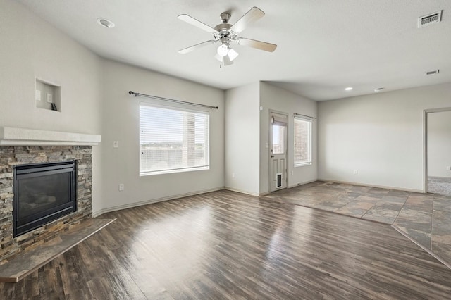 unfurnished living room featuring baseboards, a stone fireplace, ceiling fan, and wood finished floors
