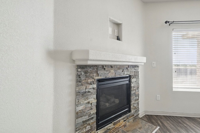 detailed view of a fireplace, wood finished floors, and baseboards