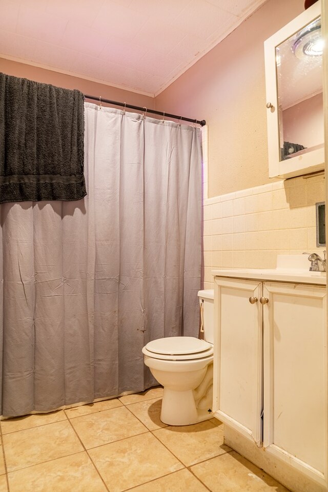 bathroom with tile patterned floors, crown molding, toilet, vanity, and tile walls