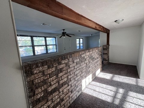 interior space with ceiling fan, brick wall, beamed ceiling, and carpet