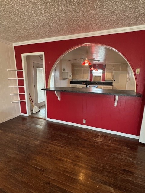 1508 W 3rd St, Fort Stockton, TX 79735 - kitchen with a textured ceiling, ornamental molding, a kitchen bar, dark countertops, and dark wood-style floors
