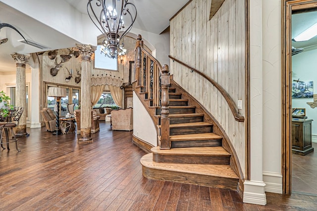 staircase with ornate columns, wooden walls, hardwood / wood-style flooring, an inviting chandelier, and a high ceiling