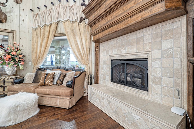 living room with dark hardwood / wood-style floors, wooden walls, and a tiled fireplace