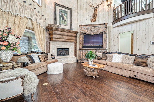 living room with a stone fireplace, wood walls, a high ceiling, and hardwood / wood-style flooring