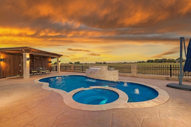 pool at dusk featuring an in ground hot tub, pool water feature, and a patio