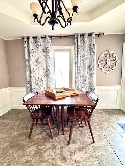 dining area with an inviting chandelier, ornamental molding, and a raised ceiling