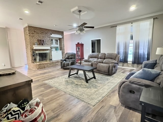 living room with crown molding, a fireplace, ceiling fan, and light wood-type flooring