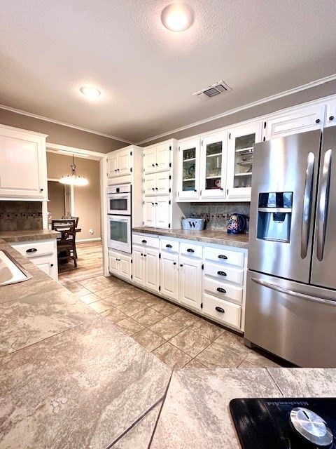 kitchen featuring stainless steel refrigerator with ice dispenser, white cabinetry, double oven, and tasteful backsplash