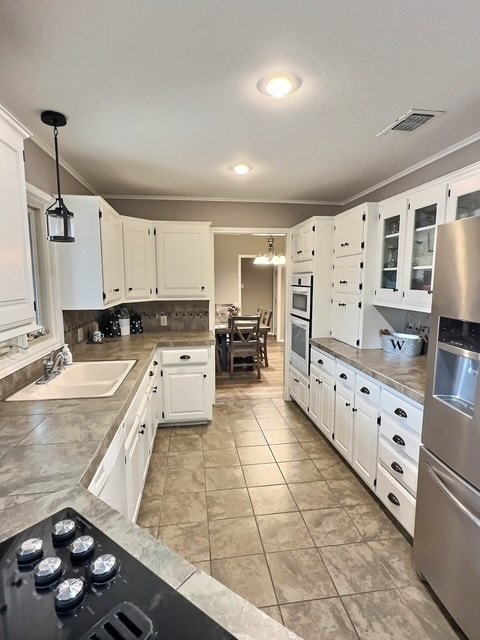 kitchen with stainless steel appliances, white cabinetry, light tile patterned flooring, and decorative light fixtures