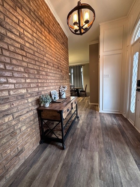 foyer featuring an inviting chandelier, ornamental molding, brick wall, and dark hardwood / wood-style floors