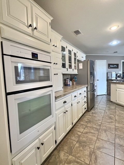 kitchen featuring stainless steel fridge, white cabinets, and white double oven