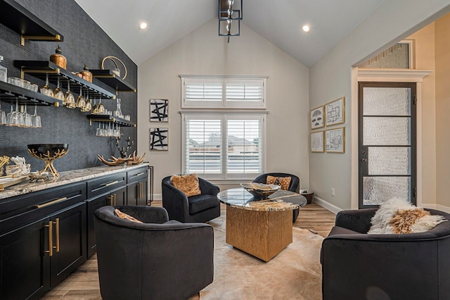 interior space with high vaulted ceiling, baseboards, light wood-style floors, backsplash, and a bar