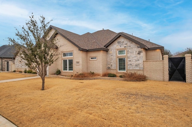 french country style house featuring a front yard, stone siding, brick siding, and roof with shingles