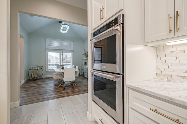 kitchen featuring light stone counters, stainless steel double oven, white cabinets, and decorative backsplash