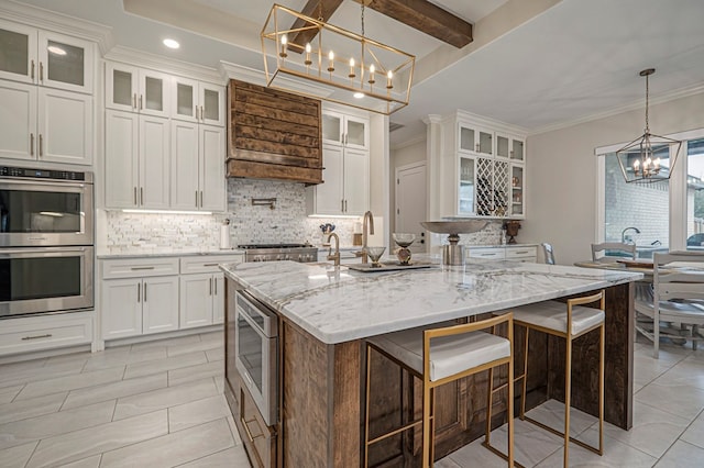 kitchen with stainless steel appliances, glass insert cabinets, a kitchen island with sink, white cabinets, and light stone countertops