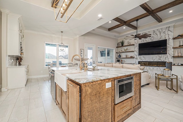 kitchen featuring a premium fireplace, open floor plan, a kitchen island with sink, white cabinetry, and light stone countertops