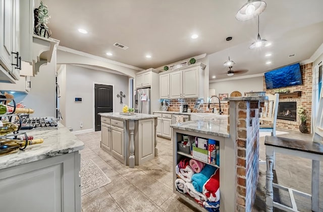 kitchen with sink, hanging light fixtures, stainless steel fridge, a kitchen island, and light stone counters