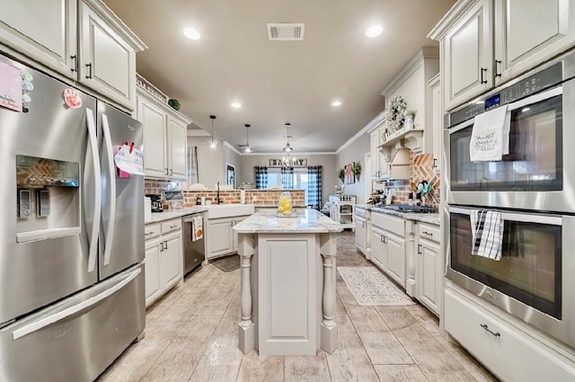 kitchen with kitchen peninsula, appliances with stainless steel finishes, backsplash, a kitchen island, and hanging light fixtures