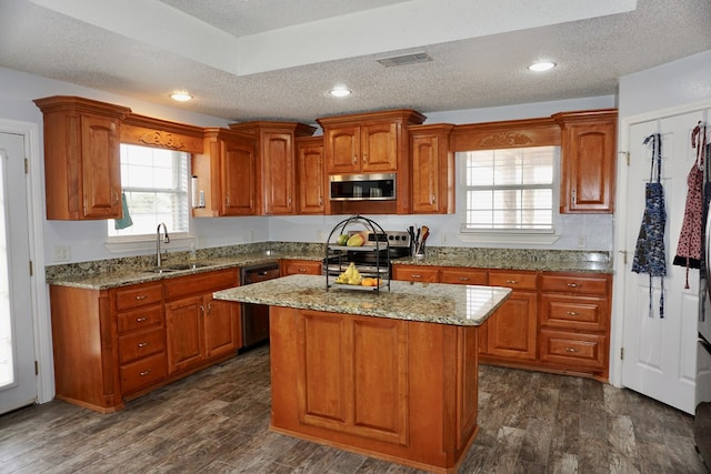 kitchen with appliances with stainless steel finishes, a sink, a textured ceiling, brown cabinetry, and visible vents