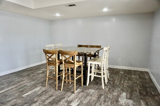 dining area with baseboards, a textured ceiling, wood finished floors, and visible vents