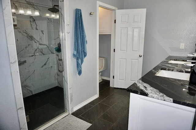 full bathroom featuring a sink, double vanity, toilet, a marble finish shower, and baseboards