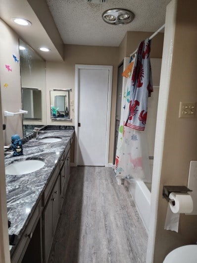 full bathroom with wood-type flooring, vanity, a textured ceiling, and shower / bathtub combination with curtain