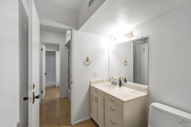 bathroom with tile patterned flooring, vanity, toilet, and a textured ceiling