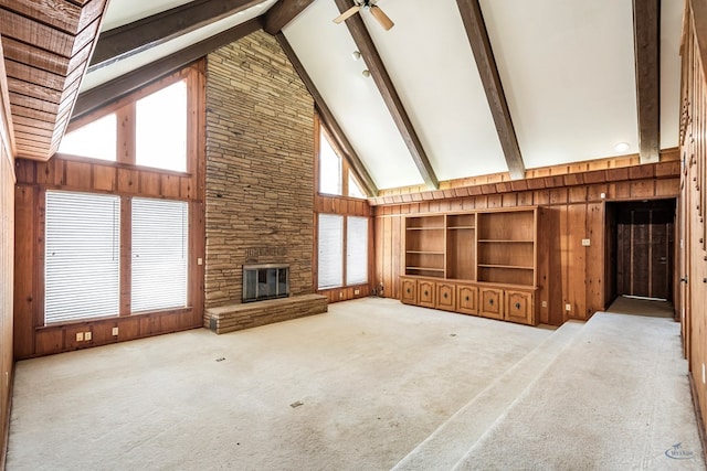 unfurnished living room with a fireplace, ceiling fan, high vaulted ceiling, beamed ceiling, and wood walls