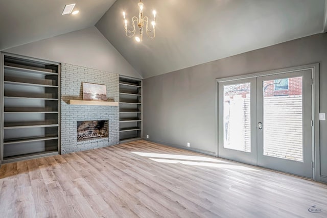 unfurnished living room with vaulted ceiling, built in features, a notable chandelier, light wood-type flooring, and a brick fireplace