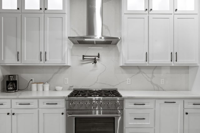 kitchen with stainless steel stove, white cabinetry, and wall chimney range hood