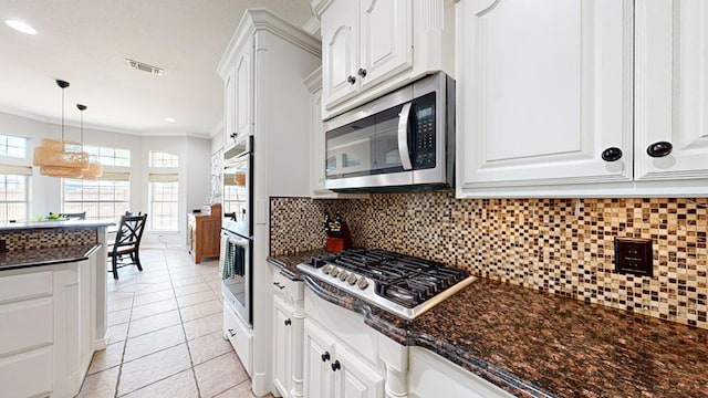 kitchen with appliances with stainless steel finishes, tasteful backsplash, ornamental molding, light tile patterned floors, and white cabinetry