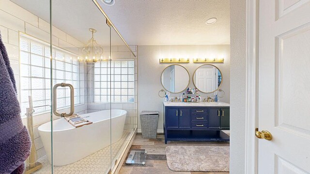 bathroom with an inviting chandelier, a bath, wood-type flooring, a textured ceiling, and vanity