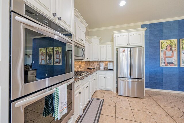 kitchen featuring light tile patterned flooring, crown molding, dark stone counters, white cabinets, and appliances with stainless steel finishes