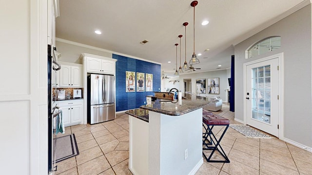 kitchen featuring white cabinetry, stainless steel fridge, pendant lighting, a kitchen bar, and a center island with sink