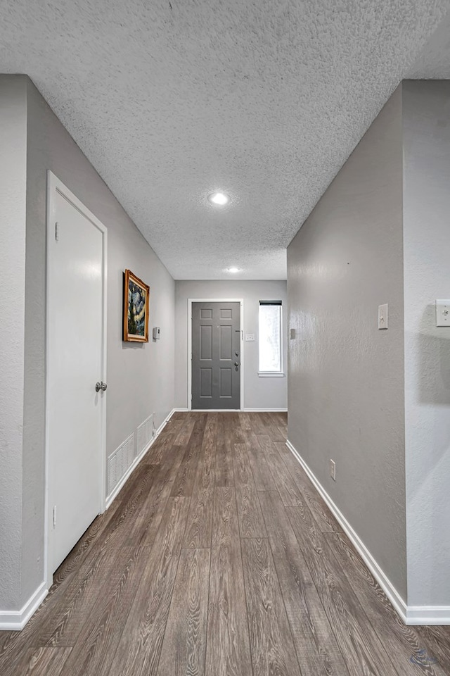 foyer featuring a textured ceiling, a textured wall, dark wood finished floors, and baseboards