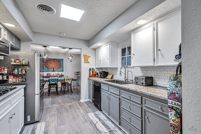 kitchen with stainless steel appliances, visible vents, white cabinets, a sink, and wood finished floors