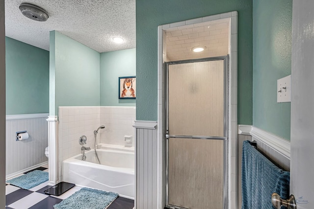 bathroom featuring a textured ceiling, a garden tub, toilet, wainscoting, and a shower stall